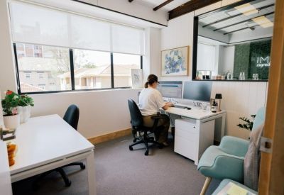 Private internal office suite featuring two white desks and a view into a common area.