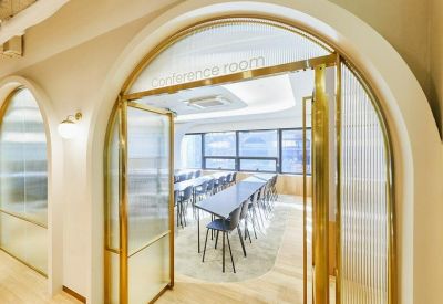 Bright conference room with a long dark table viewed through an arched doorway with gold-trimmed glass doors.