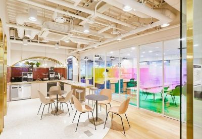 Modern coworking space featuring café seating and a vibrant glass-walled office area with green and pink accents.