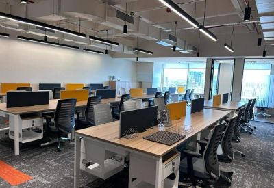 Bright open-plan office featuring wooden desks with grey and yellow privacy dividers and black mesh chairs.
