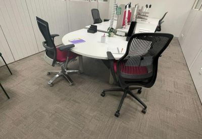 Modern open-plan office featuring curved white desks and ergonomic black chairs.