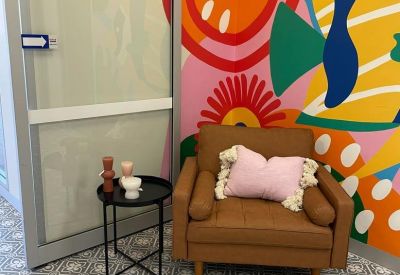 Private seating nook with a tan armchair set against a vibrant abstract wall mural.