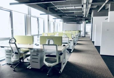 Bright open-plan workspace with white desks, ergonomic mesh chairs, and large windows providing natural light.