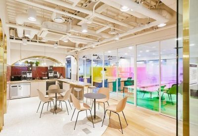 Cafe-style seating area with small round tables and colorful glass partitioned meeting rooms.