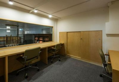 Dedicated workstation area with wooden desks and ergonomic chairs overlooking a library.