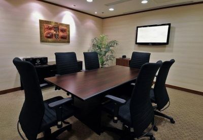 Executive meeting room with a dark wood table, black chairs, and wall-mounted screen.