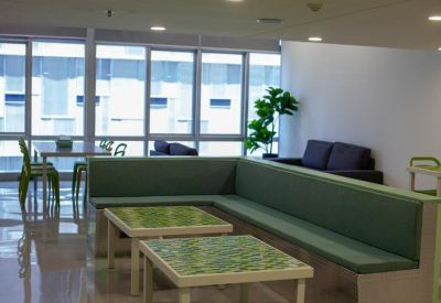 Communal lounge area with green banquette seating, tiled tables, and large windows.