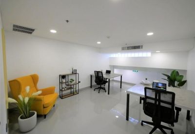 Bright open-plan workspace with multiple desks, a yellow wingback armchair, and potted plants.