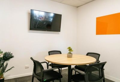 Small meeting room with a round wooden table, four chairs, and a wall-mounted TV.