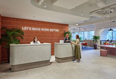 Modern reception area with concrete desks, a red brick feature wall, and green indoor plants.