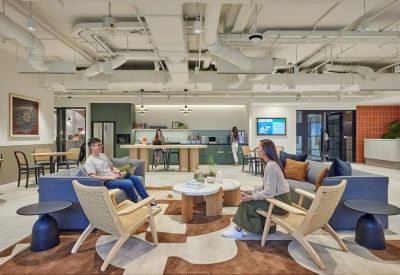 Bright breakout lounge with blue sofas, modern armchairs, and a view into a communal kitchen area.