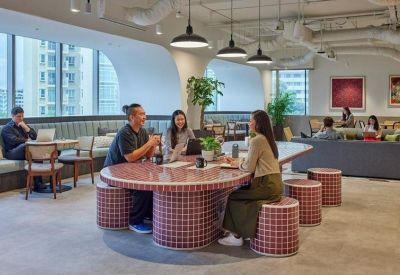 Coworking space featuring a large pink tiled table, stools, and cafe-style seating by large windows.