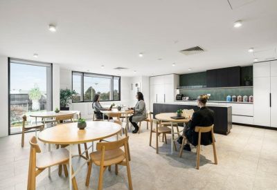 Spacious communal breakout area with dining tables, kitchenette and large windows.