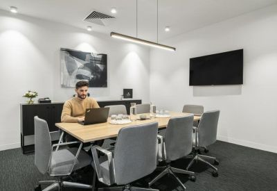 Formal boardroom with a light wood table, grey ergonomic chairs and a wall-mounted TV.