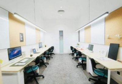 Bright open-plan office with long white desks, teal chairs, and sleek overhead strip lighting.