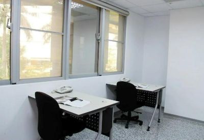 Internal two-person office suite with white desks, black rolling chairs, and large windows.