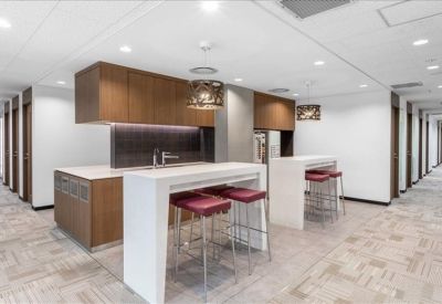 Breakout kitchen area with wooden cabinetry and high white bar tables with red stools.