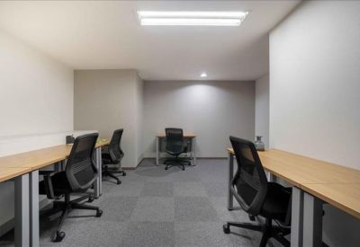Brightly lit internal workspace with multiple wooden desks and black ergonomic chairs.