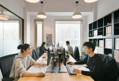 Bright open-plan workspace with long wooden desks and ergonomic seating.