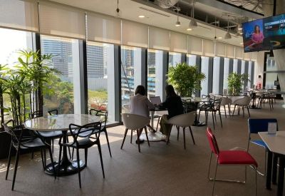 Sun-drenched communal cafe with round tables, designer chairs, and floor-to-ceiling city views.