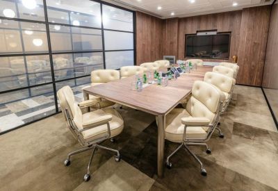 Meeting room with a long wooden table, cream-colored tufted chairs, and glass partition walls.