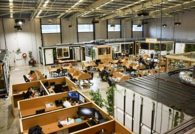 Large open-plan warehouse office with numerous wooden desks and overhead lighting.