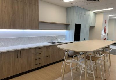 Office kitchen and break area with wooden cabinetry and a high dining table with stools.