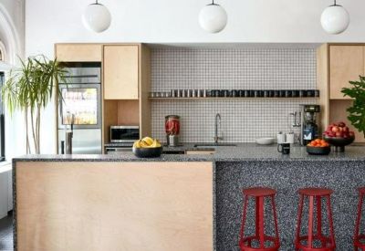Modern communal kitchen with wooden cabinetry, a grey speckled breakfast bar, and red bar stools.