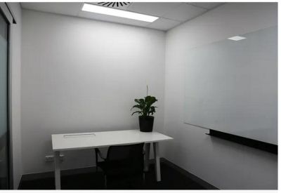Minimalist private office with a white desk, potted plant, and large glass whiteboard.