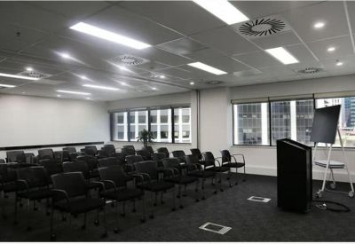 Spacious seminar room with rows of black chairs, a lectern, and large windows with city views.