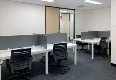 Open-plan workspace with multiple white desks, grey dividers, and black ergonomic chairs.