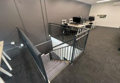 Staircase leading to an upper-level workspace with black metal railings and grey carpeting.