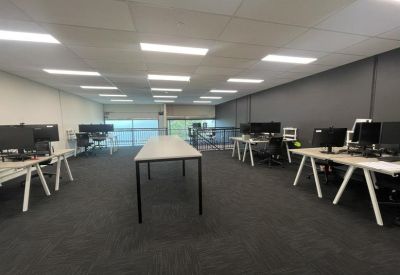 Large open-plan office with multiple rows of white desks, monitors, and overhead lighting.