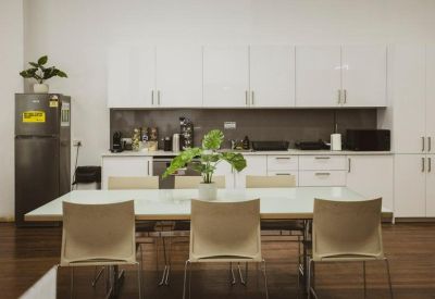 Communal kitchen area with white cabinetry, a large dining table, and potted greenery.