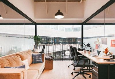Modern office space with a tan sofa and long wooden desks overlooking an atrium.