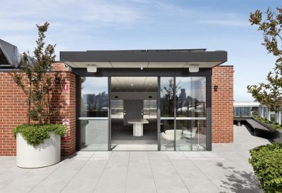 Rooftop terrace featuring red brick walls, large planters, and glass doors to an indoor lounge.