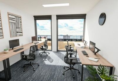 Spacious office workspace with dual windows, multiple desks, and framed wall art.