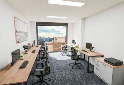 Modern workspace with long timber desks, ergonomic chairs, and a large city-facing window.