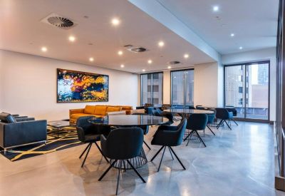 Bright communal lounge and dining area with colorful abstract art and blue designer chairs.