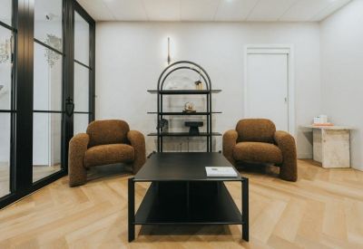Reception lounge with two brown plush armchairs and a modern black metal shelving unit.