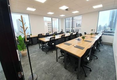 Open-plan workspace with multiple rows of wooden desks and large windows.
