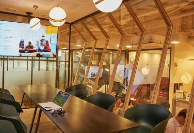 Long dark wood meeting table with green ergonomic chairs and glass partitions.