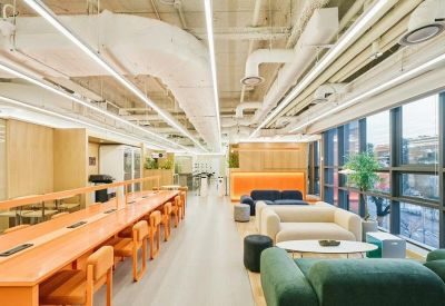 Open-plan coworking space featuring long orange desks and comfortable green velvet sofas.