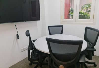 Small meeting room with a round white table, four mesh chairs, and a wall-mounted screen.