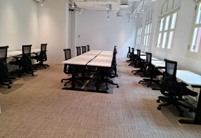 Coworking area with rows of white desks and black mesh ergonomic chairs.