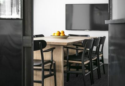 Modern meeting room with a wooden table, black chairs, and a wall-mounted screen.