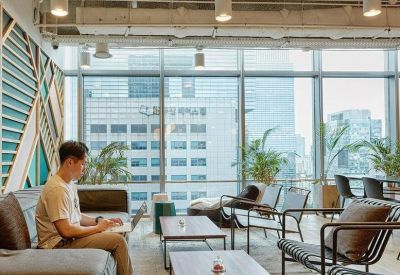 Spacious lounge area with large windows, city views, and a person working on a laptop.