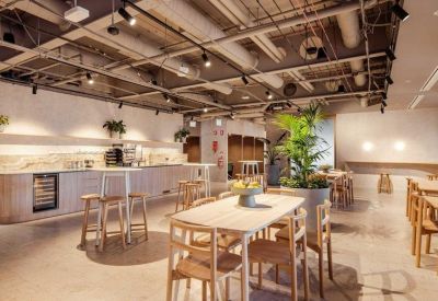 Communal kitchen and dining area with wooden tables, bar stools, and overhead track lighting.