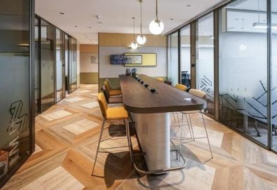 Long wooden hot-desk station in a bright corridor with glass-walled private offices.