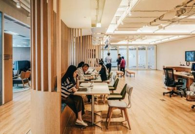 Busy coworking hub with people working at white tables under bright, industrial-style lighting.
